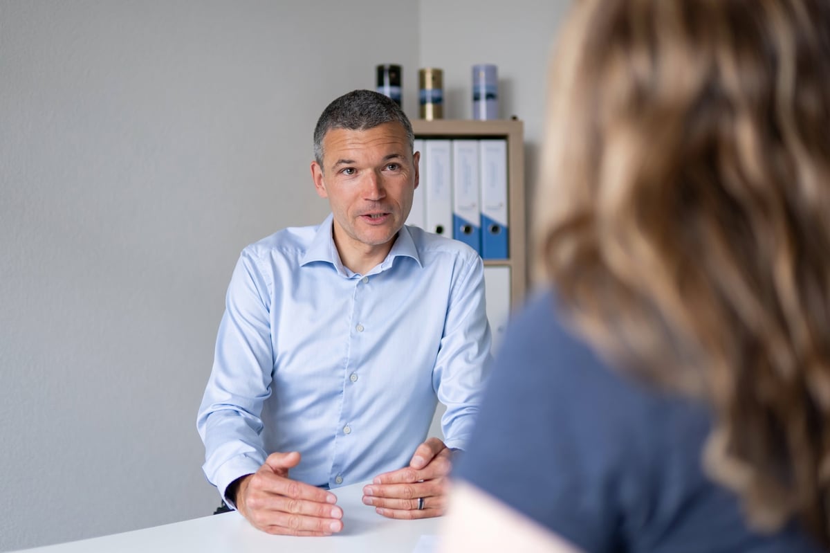 Male professional in light blue shirt speaking with woman at desk during office meeting or counseling session